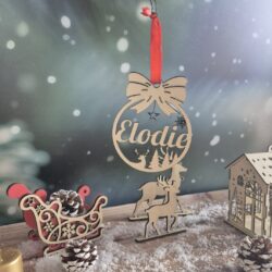 Boule de Noël en bois avec le prénom Elodie découpé, suspendue devant un fond enneigé