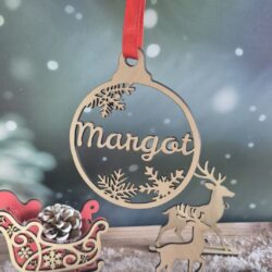 Boule de Noël en bois avec le prénom Margot découpé, suspendue devant un fond enneigé