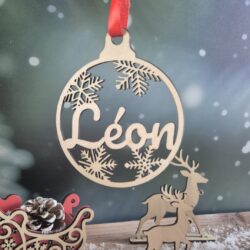Boule de Noël en bois avec le prénom Léon découpé, suspendue devant un fond enneigé