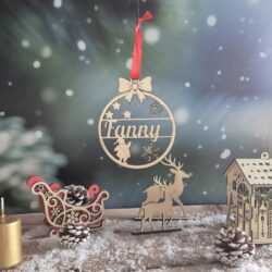 Boule de Noël en bois avec le prénom Fanny découpé, suspendue devant un fond enneigé