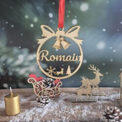 Boule de Noël en bois avec le prénom Romain découpé, suspendue devant un fond enneigé