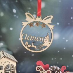 Boule de Noël en bois avec le prénom Clément découpé, suspendue devant un fond enneigé