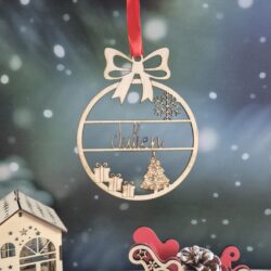 Boule de Noël en bois avec le prénom Julien découpé, suspendue devant un fond enneigé