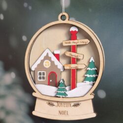 Décoration de Noël en bois représentant une maison enneigée et des panneaux gravés avec des prénoms et un nom de famille.