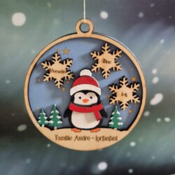 Boule de Noël en bois avec un pingouin, trois flocons gravés de prénoms et un nom de famille.